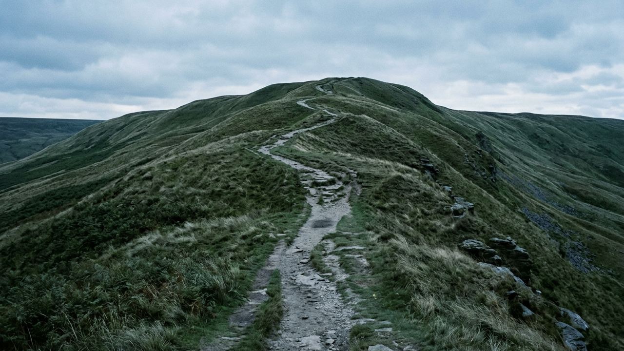 A worn footpath climbing a grassy ridge in a series of receding zigzags, stone underfoot, low sun